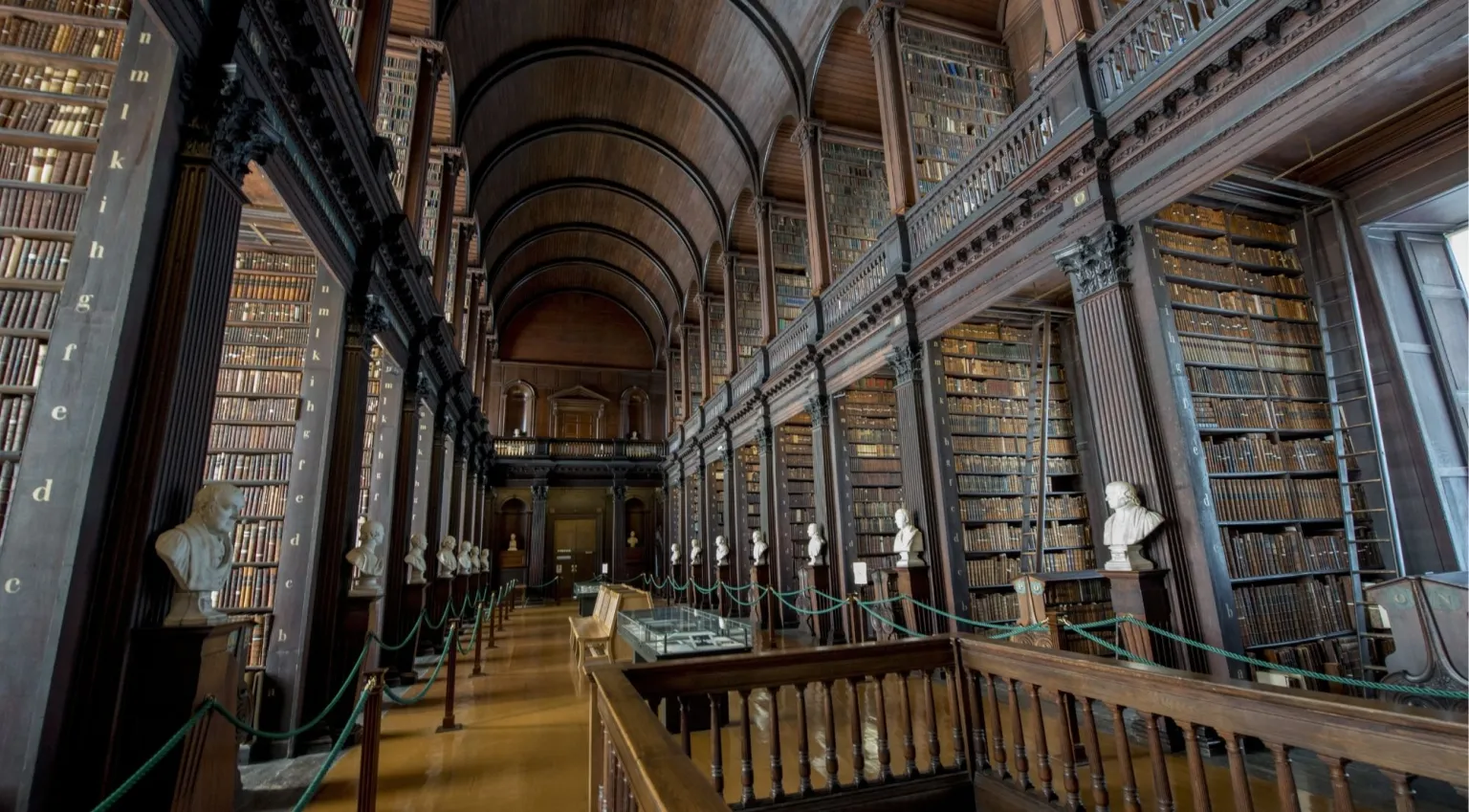 Long Room interior showing marble scholar busts and towering oak bookshelves along the vaulted corridor